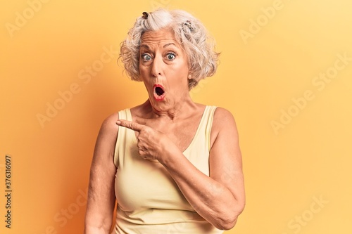 Senior grey-haired woman wearing casual clothes surprised pointing with finger to the side, open mouth amazed expression.