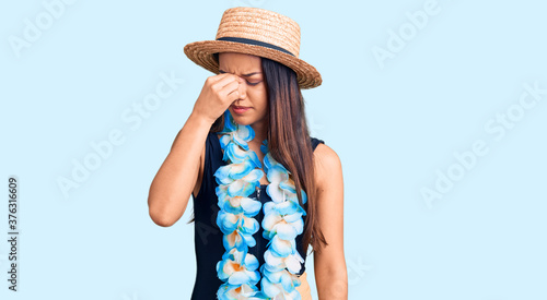 Fotografía Young beautiful latin girl wearing hawaiian lei and summer hat tired rubbing nose and eyes feeling fatigue and headache