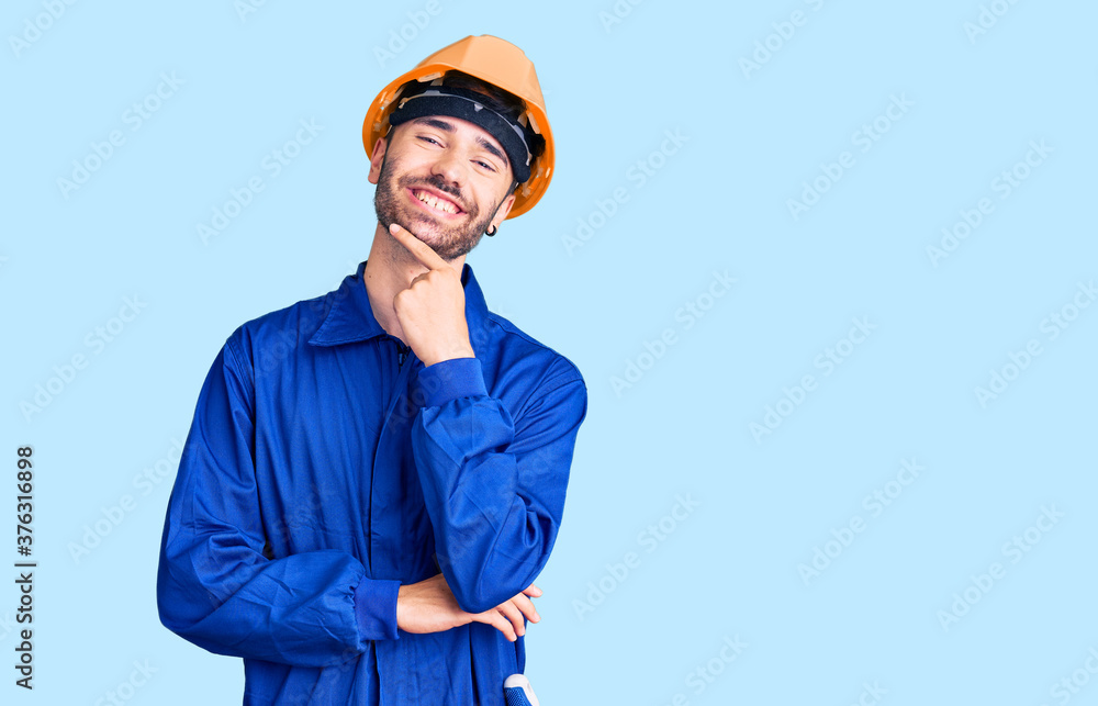 Young hispanic man wearing worker uniform looking confident at the camera smiling with crossed arms and hand raised on chin. thinking positive. Young hispanic man wearing worker uniform looking confident at the camera smiling with crossed arms and hand raised on chin. thinking positive.