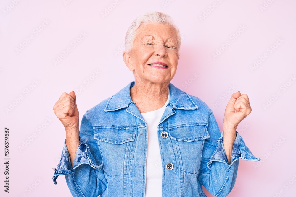Senior beautiful woman with blue eyes and grey hair wearing casual denim jacket very happy and excited doing winner gesture with arms raised, smiling and screaming for success. celebration concept. Senior beautiful woman with blue eyes and grey hair wearing casual denim jacket very happy and excited doing winner gesture with arms raised, smiling and screaming for success. celebration concept.