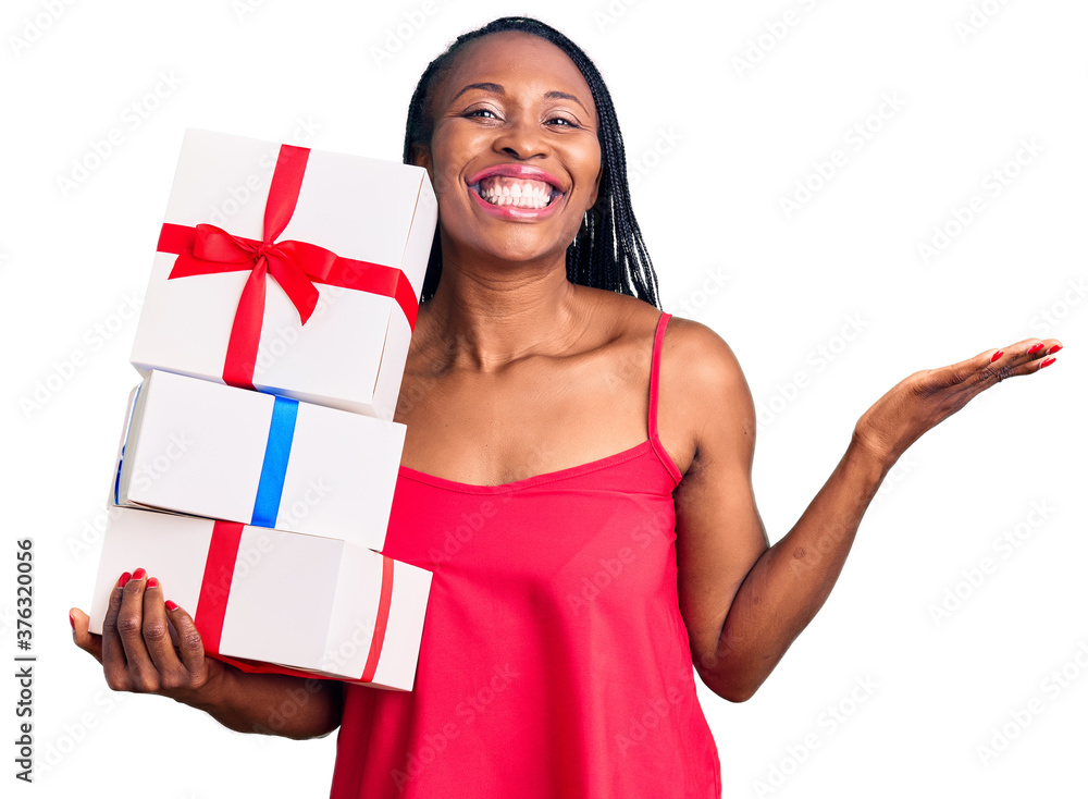 Young african american woman holding gift celebrating victory with happy smile and winner expression with raised hands Young african american woman holding gift celebrating victory with happy smile and winner expression with raised hands