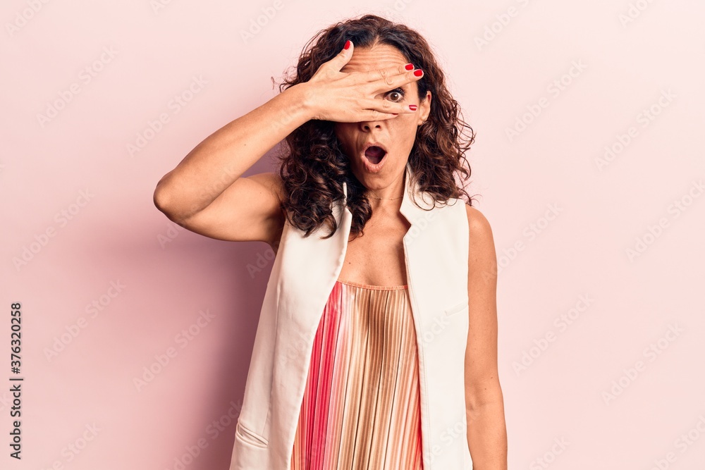 Middle age beautiful woman wearing casual vest peeking in shock covering face and eyes with hand, looking through fingers afraid Middle age beautiful woman wearing casual vest peeking in shock covering face and eyes with hand, looking through fingers afraid