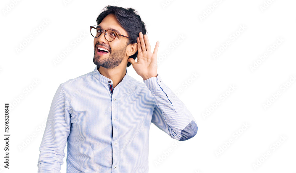 Handsome hispanic man wearing business shirt and glasses smiling with hand over ear listening an hearing to rumor or gossip. deafness concept. Handsome hispanic man wearing business shirt and glasses smiling with hand over ear listening an hearing to rumor or gossip. deafness concept.