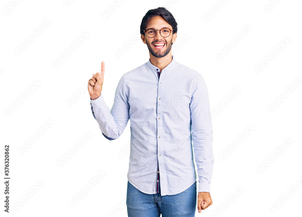 Handsome hispanic man wearing business shirt and glasses showing and pointing up with finger number one while smiling confident and happy. Handsome hispanic man wearing business shirt and glasses showing and pointing up with finger number one while smiling confident and happy.