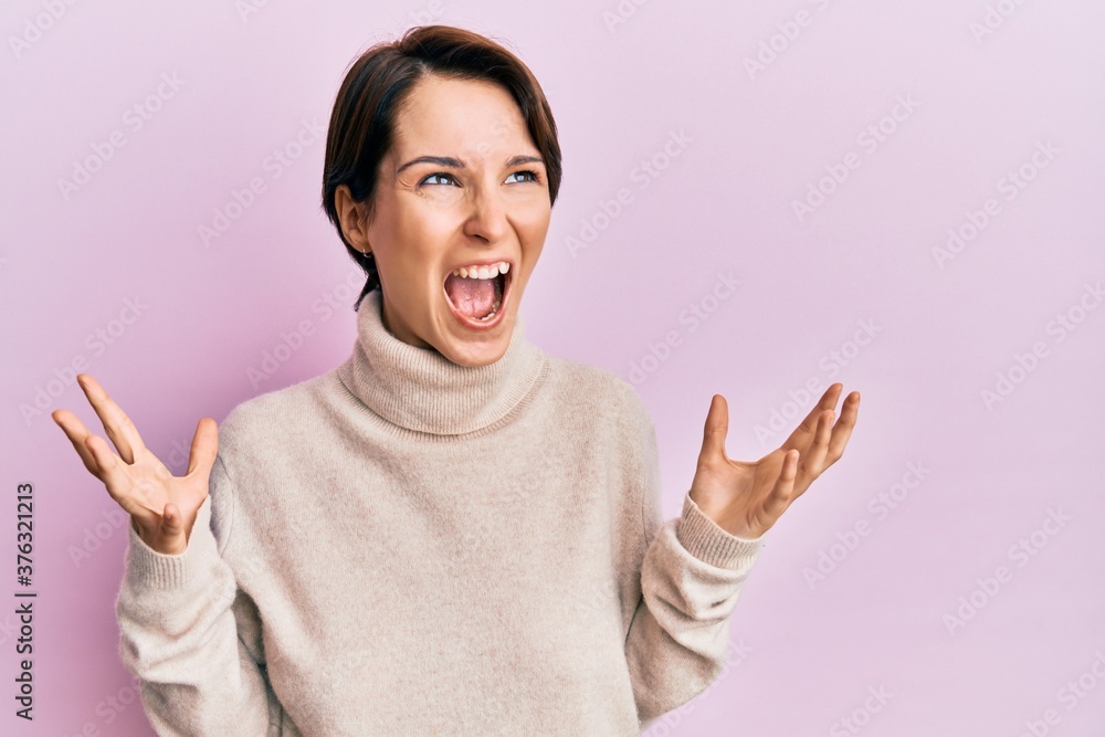 Young brunette woman with short hair wearing casual winter sweater crazy and mad shouting and yelling with aggressive expression and arms raised. frustration concept. Young brunette woman with short hair wearing casual winter sweater crazy and mad shouting and yelling with aggressive expression and arms raised. frustration concept.
