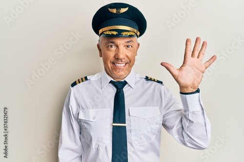 Handsome middle age mature man wearing airplane pilot uniform showing and pointing up with fingers number five while smiling confident and happy. © Krakenimages.com