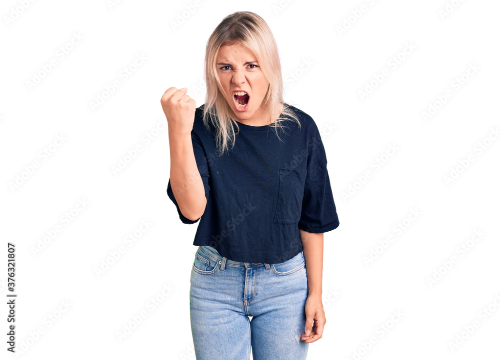Young beautiful blonde woman wearing casual t-shirt angry and mad raising fist frustrated and furious while shouting with anger. rage and aggressive concept. Young beautiful blonde woman wearing casual t-shirt angry and mad raising fist frustrated and furious while shouting with anger. rage and aggressive concept.