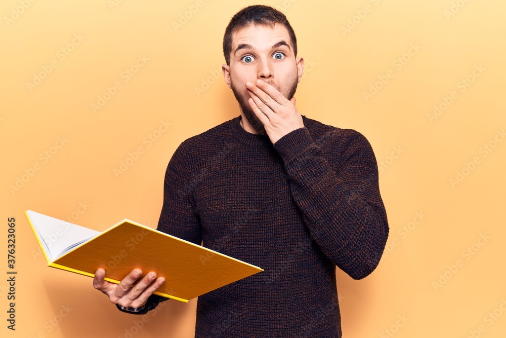 Young handsome man reading book covering mouth with hand, shocked and afraid for mistake. surprised expression Young handsome man reading book covering mouth with hand, shocked and afraid for mistake. surprised expression