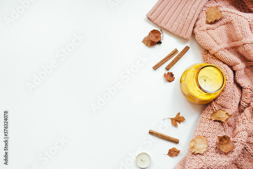 Knitted sweater, autumn leaves, cinnamon sticks, candles on white background. Autumn composition. Flat lay, top view, copy space