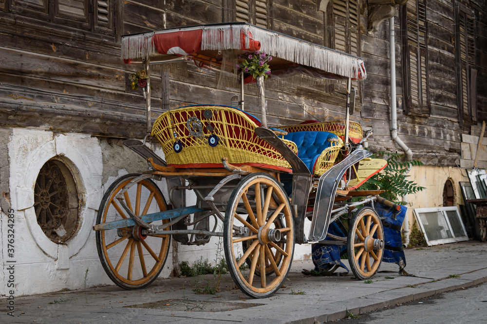 A colorful horse-drawn carriage parked in front of an old wooden house.