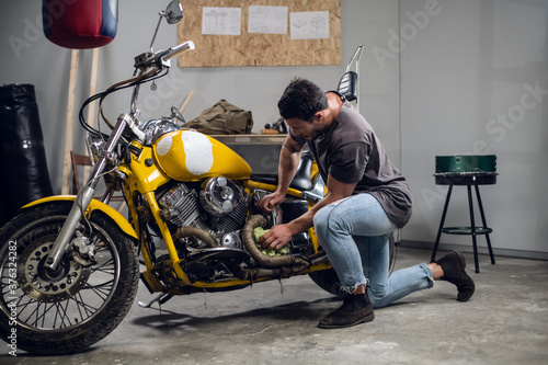 A strong male biker repairs his motorcycle in the garage. Interior of the workshop