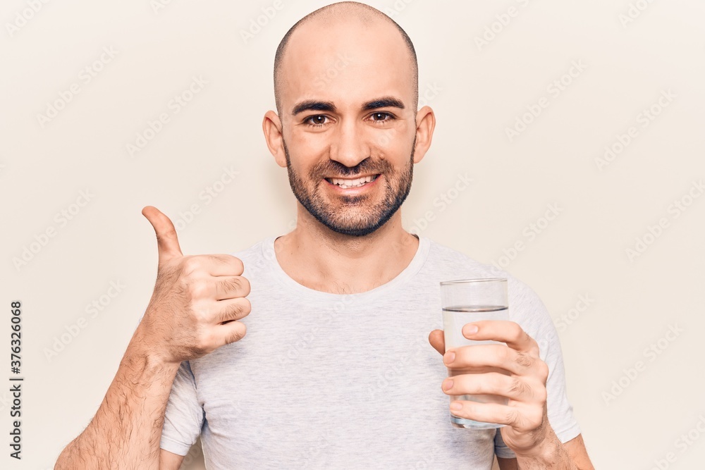 Young handsome bald man drinking glass of water smiling happy and positive, thumb up doing excellent and approval sign Young handsome bald man drinking glass of water smiling happy and positive, thumb up doing excellent and approval sign