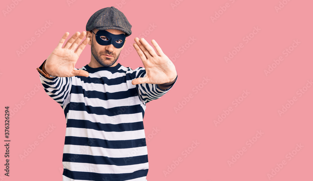 Young handsome man wearing burglar mask doing frame using hands palms and fingers, camera perspective Young handsome man wearing burglar mask doing frame using hands palms and fingers, camera perspective