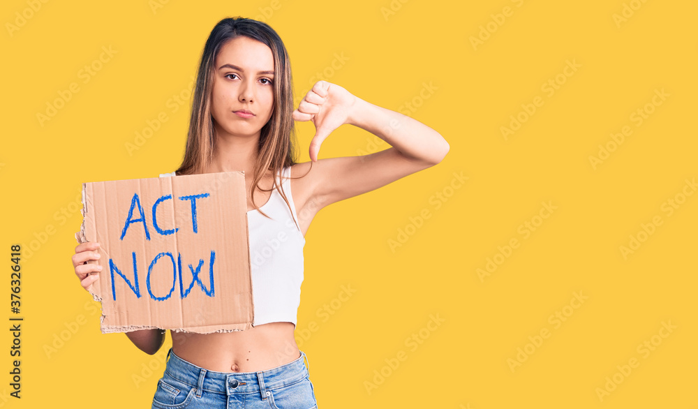 Young beautiful girl holding act now banner with angry face, negative sign showing dislike with thumbs down, rejection concept Young beautiful girl holding act now banner with angry face, negative sign showing dislike with thumbs down, rejection concept