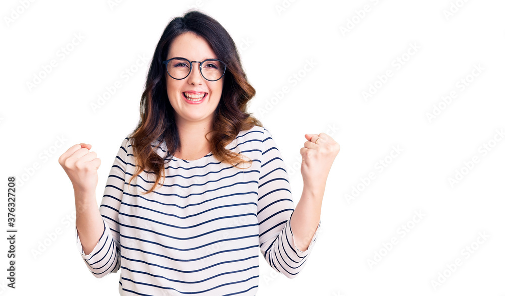 Beautiful young brunette woman wearing casual clothes and glasses celebrating surprised and amazed for success with arms raised and open eyes. winner concept. Beautiful young brunette woman wearing casual clothes and glasses celebrating surprised and amazed for success with arms raised and open eyes. winner concept.