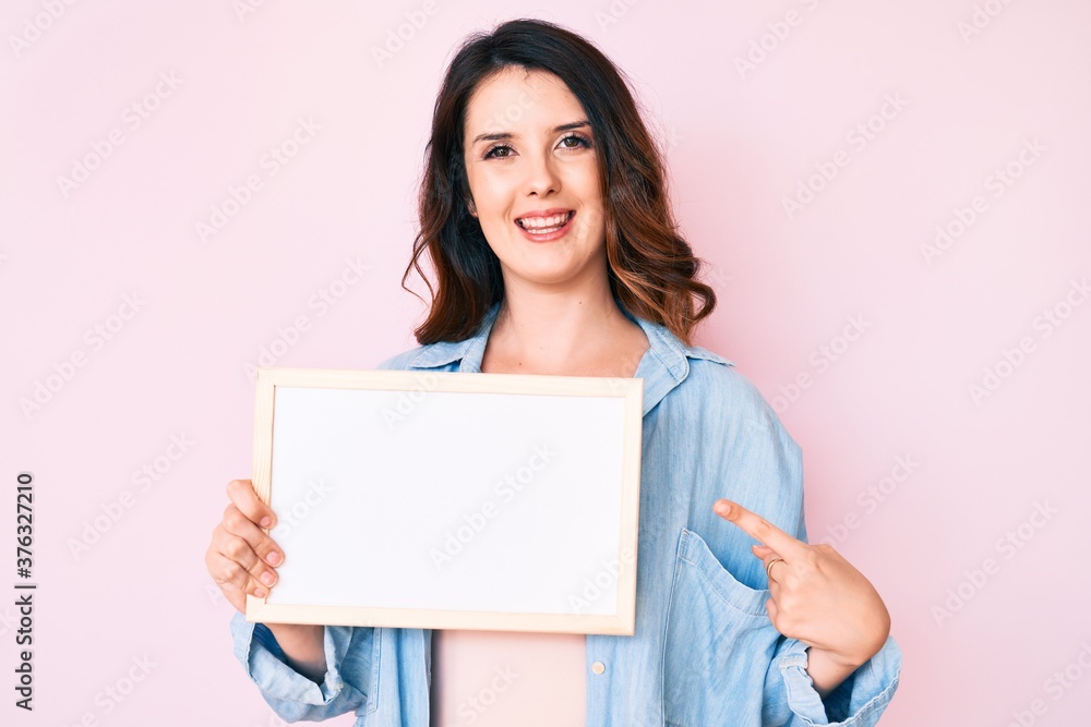 Young beautiful brunette woman holding blank empty banner smiling happy pointing with hand and finger Young beautiful brunette woman holding blank empty banner smiling happy pointing with hand and finger