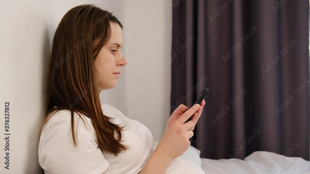 Side view of young woman wake up lying in bed spend time uses smartphone, starts new day check social networks messages, communicating with friends, review plan of day in agenda calendar concept Side view of young woman wake up lying in bed spend time uses smartphone, starts new day check social networks messages, communicating with friends, review plan of day in agenda calendar concept