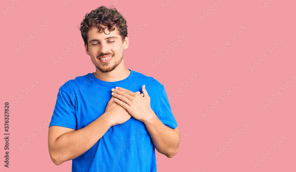 Young handsome man with curly hair wearing casual clothes smiling with hands on chest with closed eyes and grateful gesture on face. health concept. Young handsome man with curly hair wearing casual clothes smiling with hands on chest with closed eyes and grateful gesture on face. health concept.