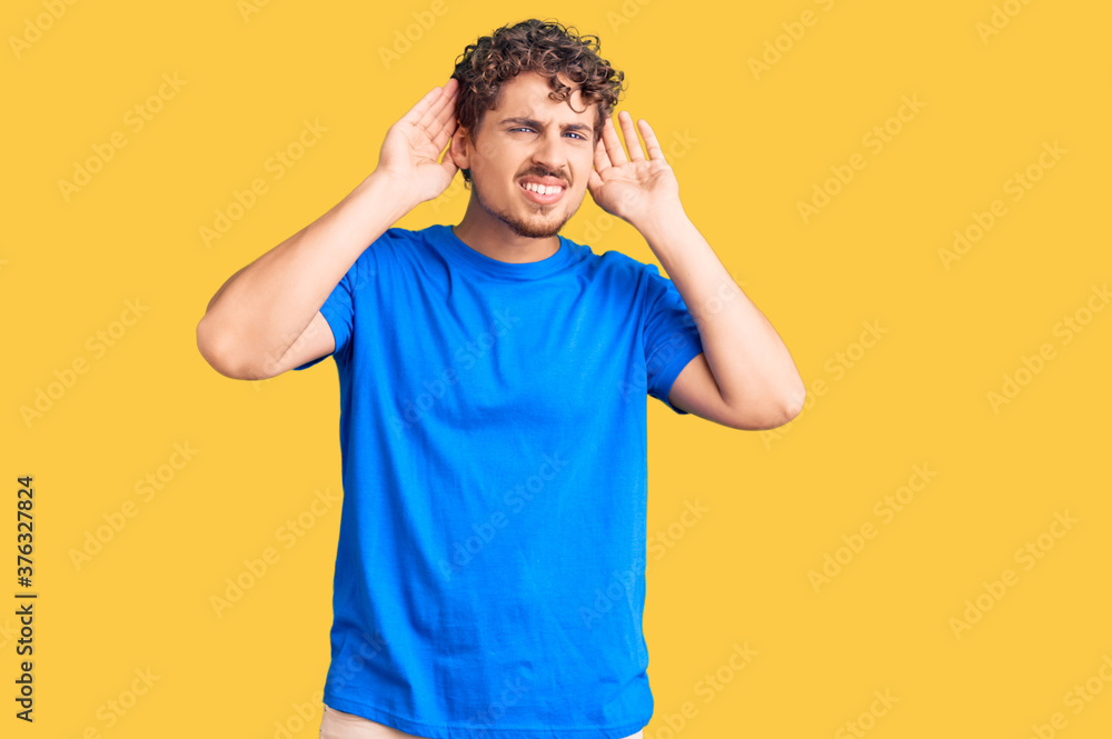 Young handsome man with curly hair wearing casual clothes trying to hear both hands on ear gesture, curious for gossip. hearing problem, deaf Young handsome man with curly hair wearing casual clothes trying to hear both hands on ear gesture, curious for gossip. hearing problem, deaf