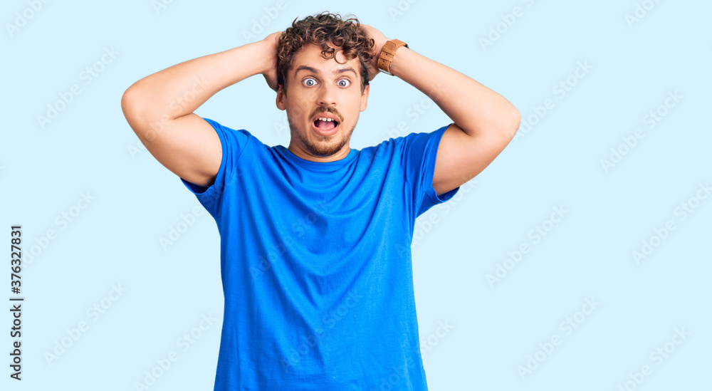 Young handsome man with curly hair wearing casual clothes crazy and scared with hands on head, afraid and surprised of shock with open mouth Young handsome man with curly hair wearing casual clothes crazy and scared with hands on head, afraid and surprised of shock with open mouth