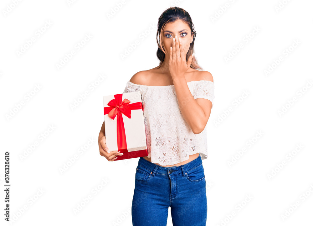 Young beautiful woman holding gift covering mouth with hand, shocked and afraid for mistake. surprised expression Young beautiful woman holding gift covering mouth with hand, shocked and afraid for mistake. surprised expression