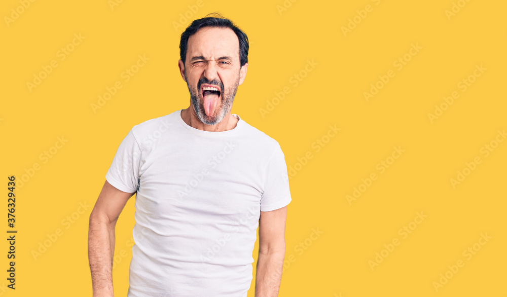 Middle age handsome man wearing casual t-shirt sticking tongue out happy with funny expression. emotion concept.