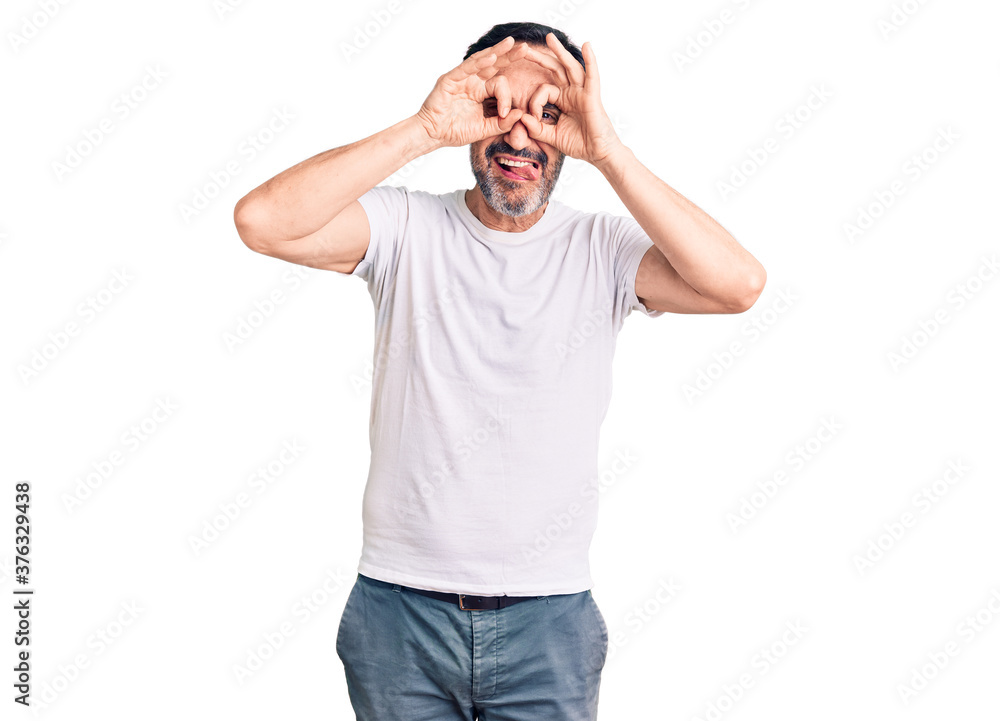 Fototapeta premium Middle age handsome man wearing casual t-shirt doing ok gesture like binoculars sticking tongue out, eyes looking through fingers. crazy expression.