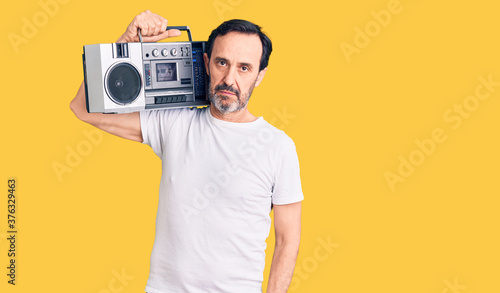 Middle age handsome man listening to music using vintage boombox thinking attitude and sober expression looking self confident