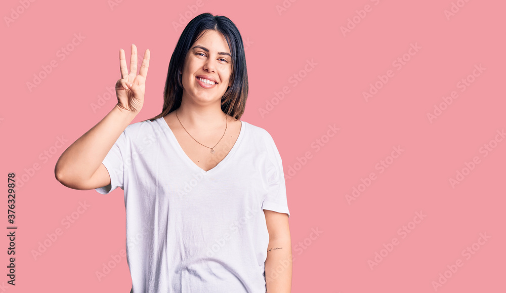 Young beautiful brunette woman wearing casual t-shirt showing and pointing up with fingers number three while smiling confident and happy. Young beautiful brunette woman wearing casual t-shirt showing and pointing up with fingers number three while smiling confident and happy.
