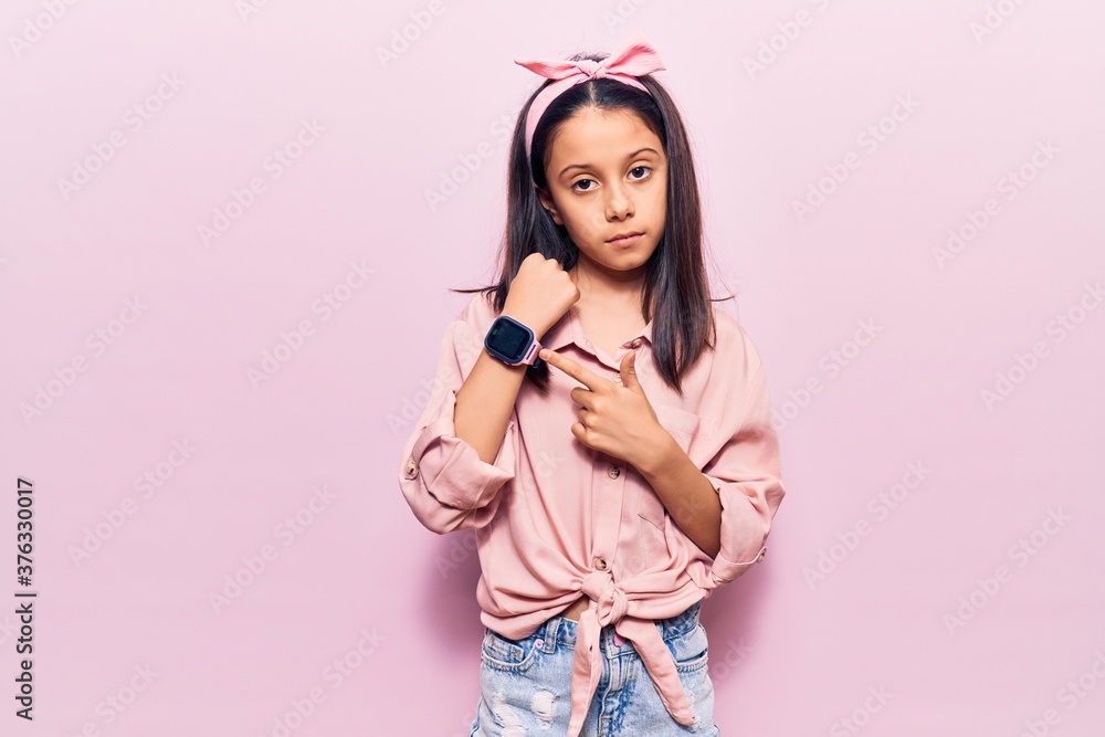 Beautiful child girl wearing casual clothes in hurry pointing to watch time, impatience, looking at the camera with relaxed expression Beautiful child girl wearing casual clothes in hurry pointing to watch time, impatience, looking at the camera with relaxed expression