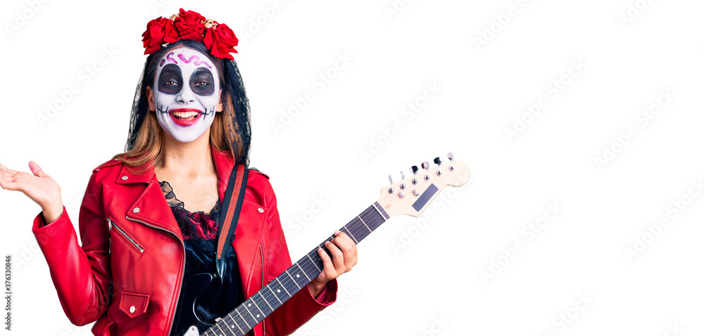 Woman wearing day of the dead costume playing electric guitar celebrating victory with happy smile and winner expression with raised hands