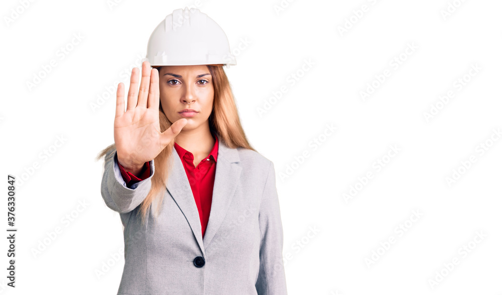 Beautiful young woman wearing architect hardhat doing stop sing with palm of the hand. warning expression with negative and serious gesture on the face. Beautiful young woman wearing architect hardhat doing stop sing with palm of the hand. warning expression with negative and serious gesture on the face.