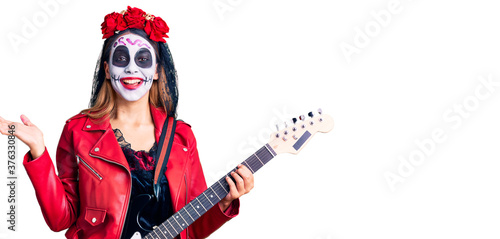 Woman wearing day of the dead costume playing electric guitar celebrating victory with happy smile and winner expression with raised hands