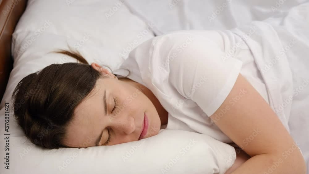 Side view close up of satisfied peaceful serene beautiful young woman lying asleep relaxing sleeping in cozy bed on soft pillow resting covered with white blanket enjoying good healthy sleep concept Side view close up of satisfied peaceful serene beautiful young woman lying asleep relaxing sleeping in cozy bed on soft pillow resting covered with white blanket enjoying good healthy sleep concept