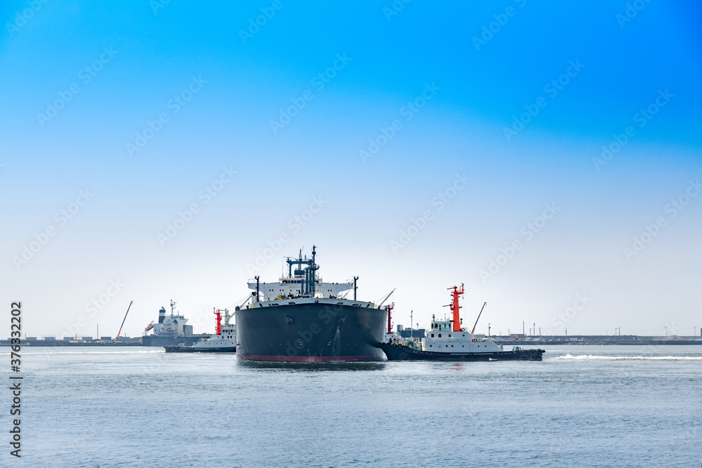 日本の港を出港する貨物船と綱取り放し作業するタグボート