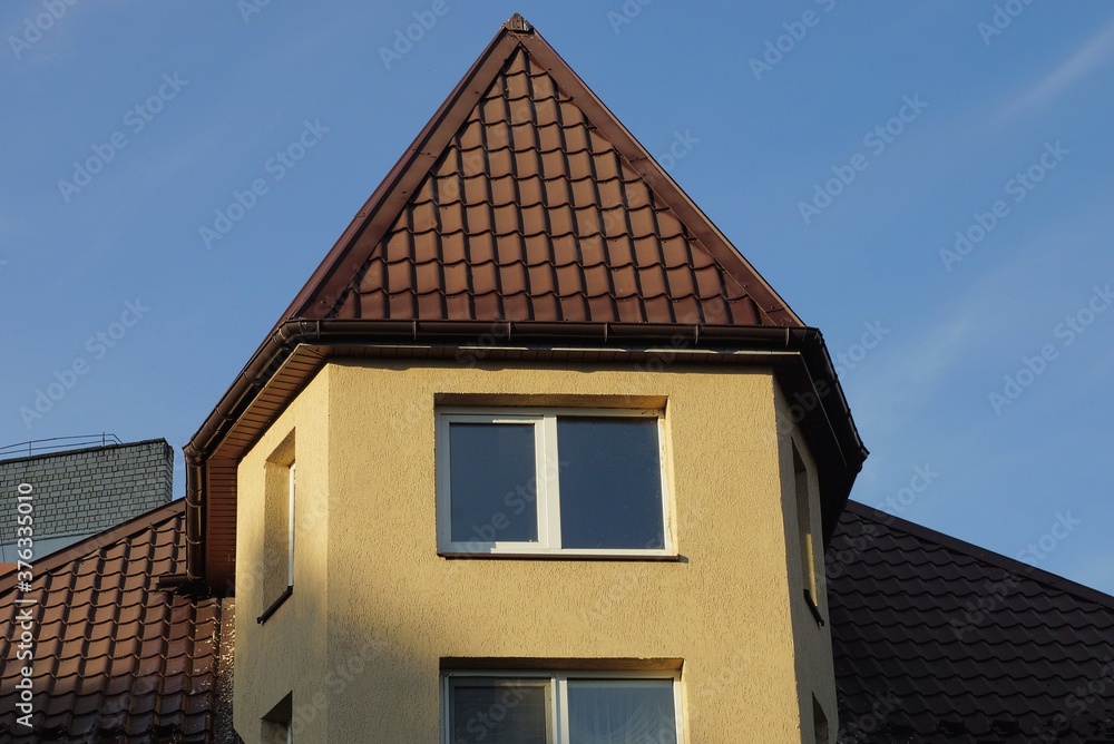 attic of a private house with windows under a brown tiled roof against a blue sky