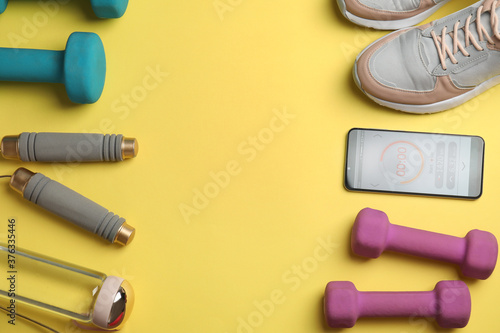 Smartphone with timer and fitness accessories on yellow background, flat lay. Space for text
