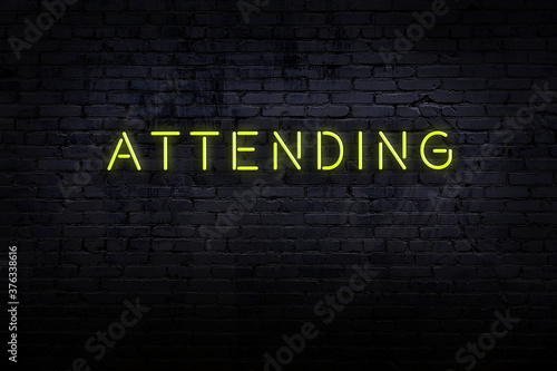 Neon sign. Word attending against brick wall. Night view