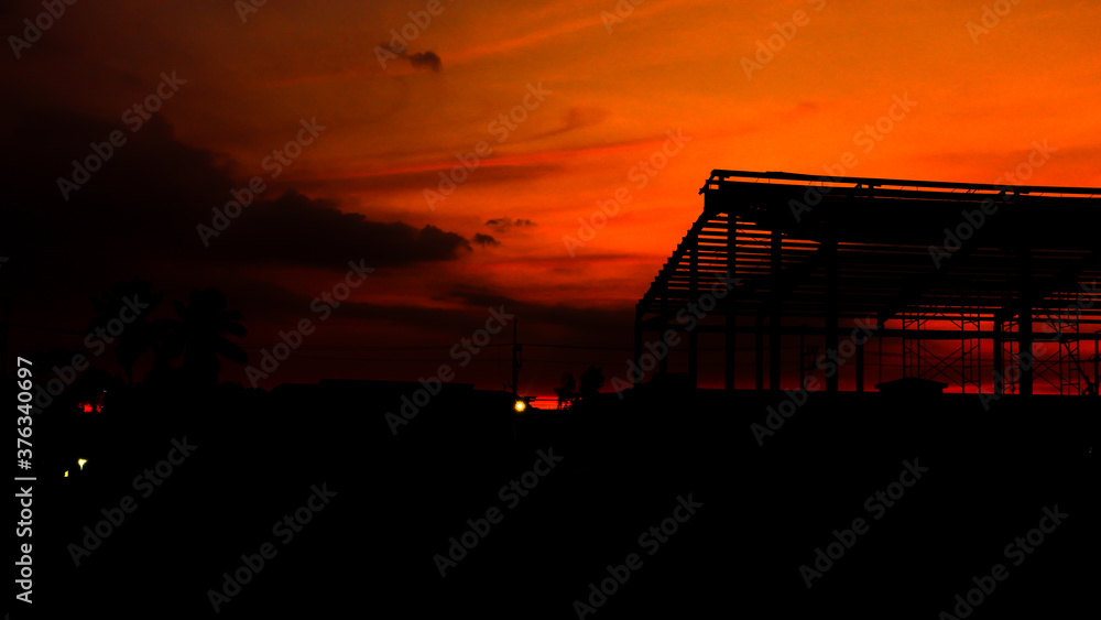 Obraz premium Orange sky during sunset with warehouse and trees silhouette