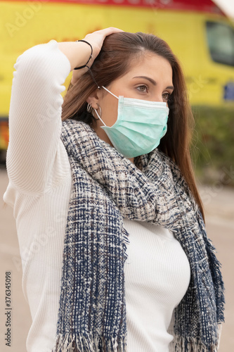 Closeup of a worried looking teenager using a green surgical mask putting her right hand behind her head