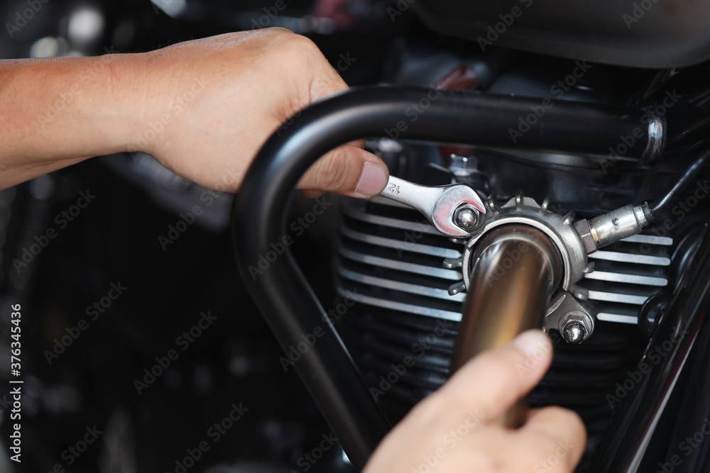 Mechanic using a wrench and socket on exhaust pipe of a motorcycle .maintenance,repair motorcycle concept in garage .selective focus