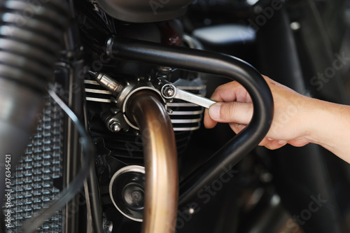 Mechanic using a wrench and socket on exhaust pipe of a motorcycle .maintenance,repair motorcycle concept in garage .selective focus © kasarp