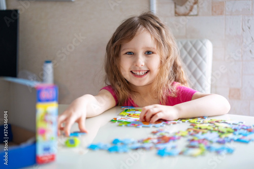 little girl with light wavy hair collects a puzzle at home and has fun.