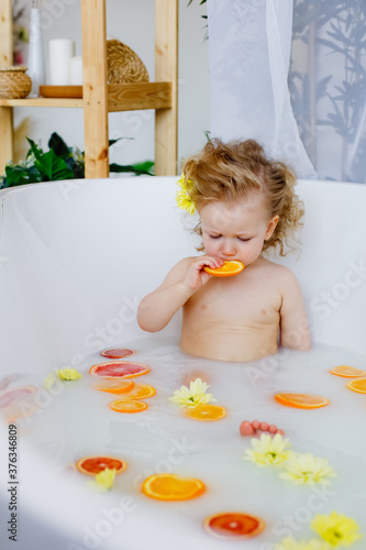 Child on the milk bath with flowersa little girl with curly hair in a milk bath with yellow flowers and orange oranges, red grapefruits. photo