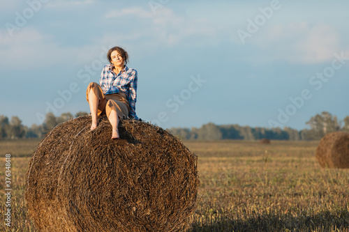 The concept of livestyle outdoor in autumn. Close up of a young woman in a warm autumn clothes looking funny, smilling, posing on the haystack