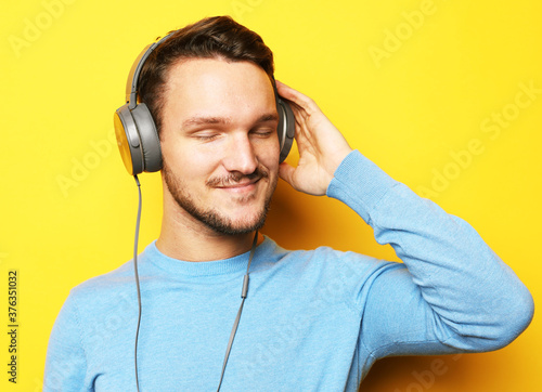 Handsome young Man, wearing blue sweater, listening to music over yellow background