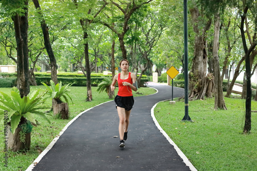 Relaxed smiling Asian fitness runner woman listening music and running workout in natural park.