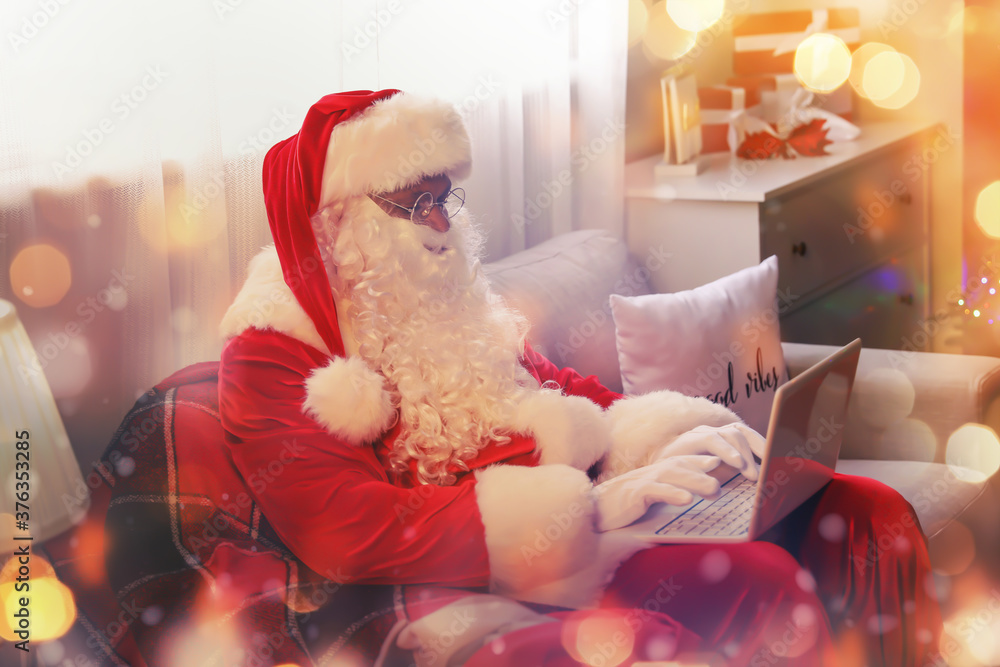 Obraz premium African-American Santa Claus with laptop in room decorated for Christmas