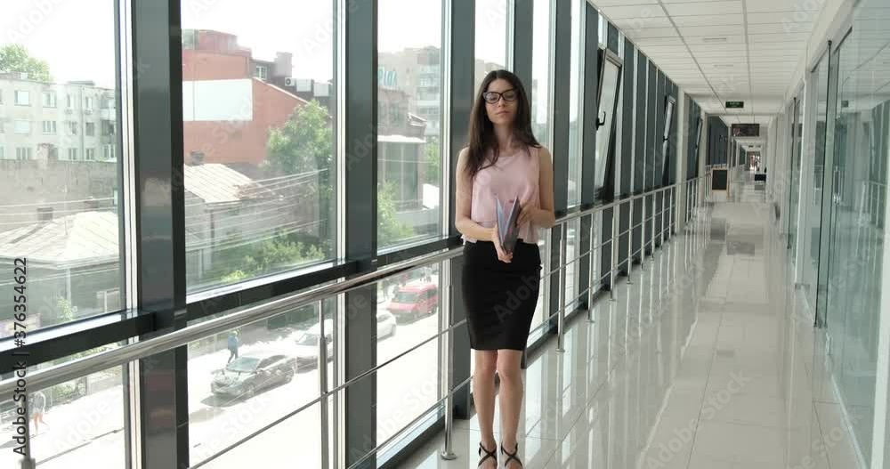 Beautiful girl in glasses with a notebook walks down the corridor of the business center Beautiful girl in glasses with a notebook walks down the corridor of the business center