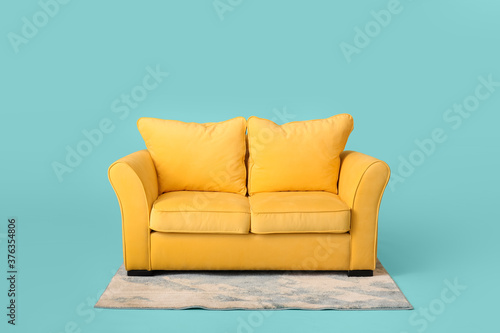 Stylish sofa and carpet on color background